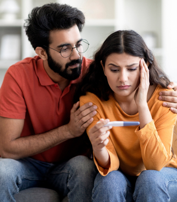 An upset young Indian couple looking at negative pregnancy.